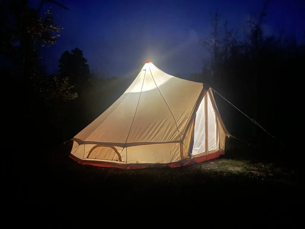 a tent in the forest at night with a light on