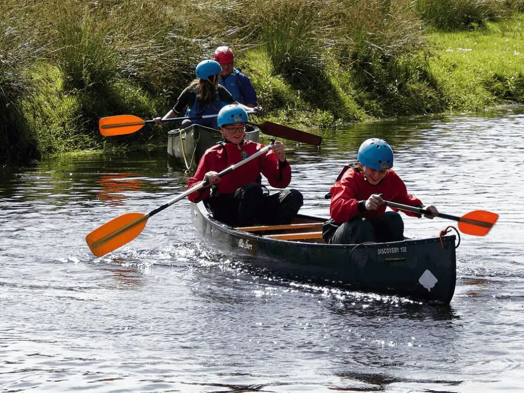 three pupils in a boat on a river with oars rowing