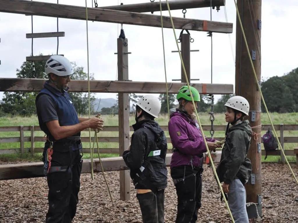students with safety gear on waiting to climb up a activity tower