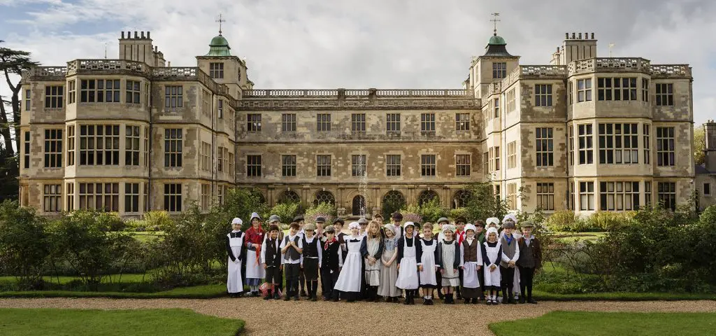 school group dressed up as servants with a manor house behind them