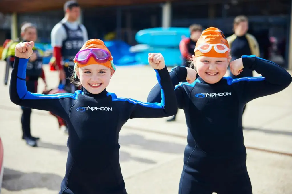 two primary school pupils having a photo taken with there wet suits googles and swimming hats on