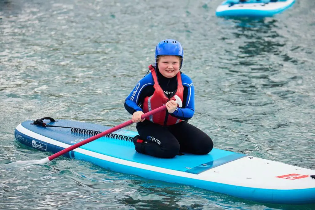 primary school pupil on a paddle board on lake with safter water proofs on