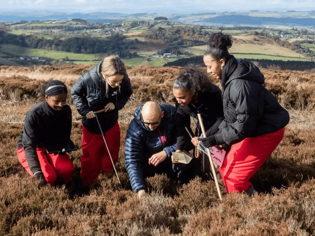 school group up on a hill looking in heather and moss doing field studies