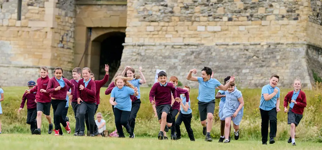 school group ruing in a field next to a middle ages castle wall and keep