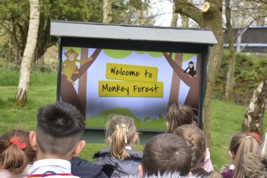 children outside looking at a signed saying welcome to monkey forest