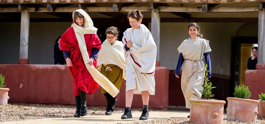 English Heritage West Midlands 6 four school pupils dressed in Roman white togas at an old roman reconstructed town house