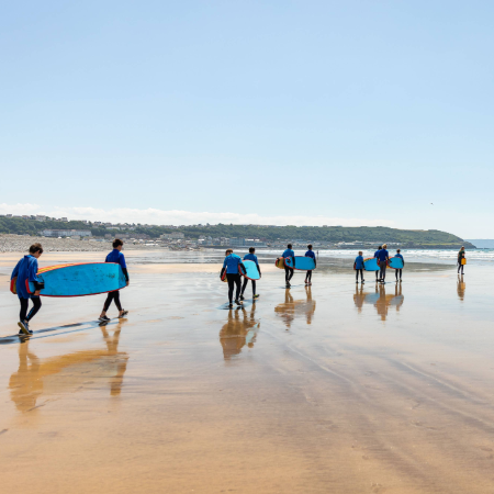 school group walking at the beach with surf boards
