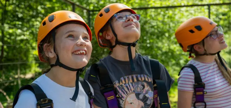 three school pupils with hard hats waiting to go on a climbing tower