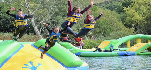 school group jumping of an inflatable object into the water on a lake