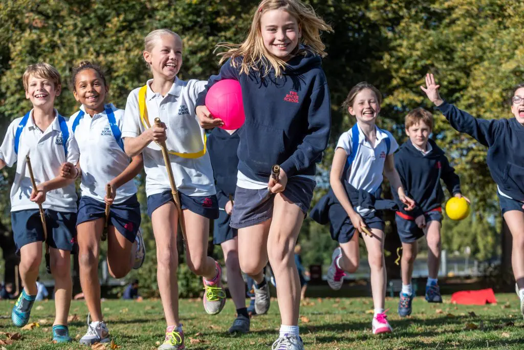 school pupils running in a field with hockey sticks and balls