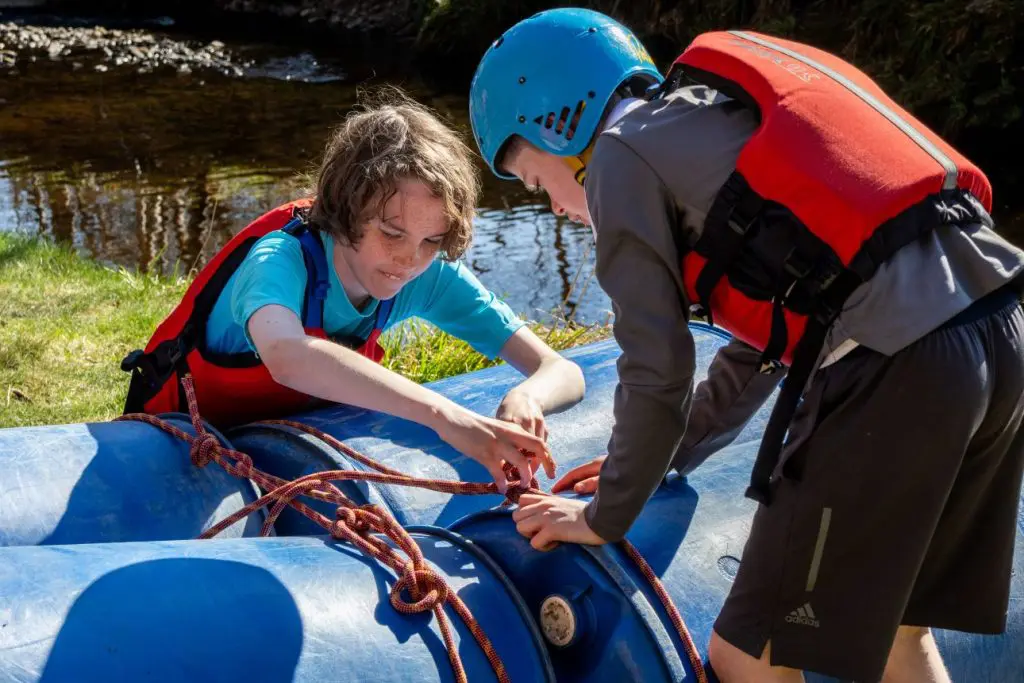 two secondary pupils tying rope around plastic blue drums making a water raft to float in the water