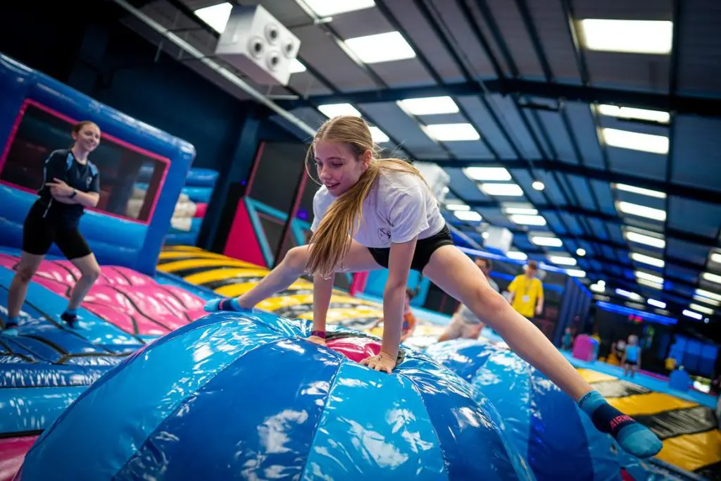 secondary school pupil doing a split jump over an inflatable object at an indoors trampoline park