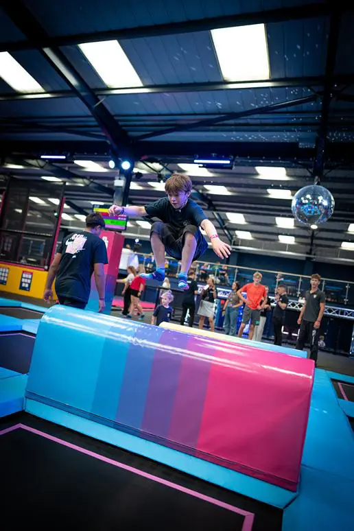 student jumping on a trampoline over an obstacle course at an indoor trampoline park