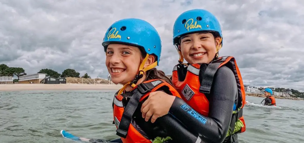 primary school pupils in the water with wet suits helmets and life jackets on smiling and having fun