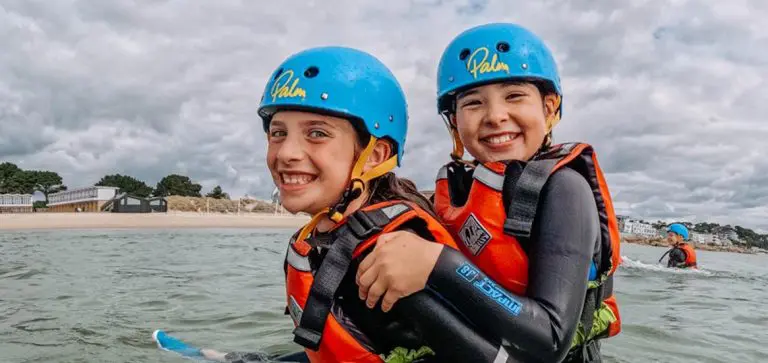 primary school pupils in the water with wet suits helmets and life jackets on smiling and having fun
