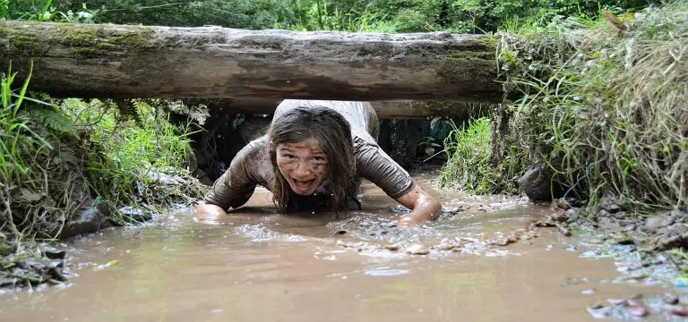 school pupil on an assault course going under a log in muddy water