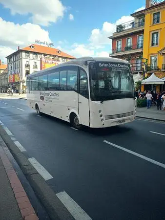 single white coach driving on a road in the centre of a town