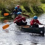 three pupils in a boat on a river with oars rowing