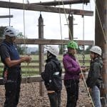 students with safety gear on waiting to climb up a activity tower