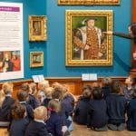 school group sitting in the floor looking at a number of paintings on the wall