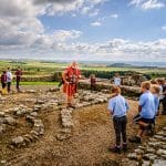 school group looking at Roman ruins of a villa with tour guide dressed as a Roman Soldier