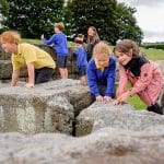 pupils outside looking at Hadrian wall made of large stone blocks