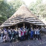 school group waving with teacher in the woods under a Celtic round house