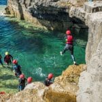 school students jumping into the sea of rocks with safety waterproofs on and hard hats