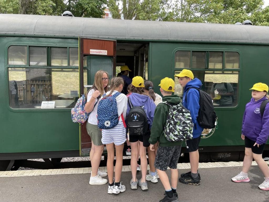 school group with teacher boarding an old fashioned steam train and carriage