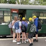 school group with teacher boarding an old fashioned steam train and carriage