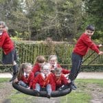 school children smiling and laughing on a large rope swing in a play area