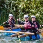 school pupils on a raft paddling on a lake with wet suits, hard hats and life jackets on