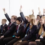 school group in a stadium room asking questions raising hands