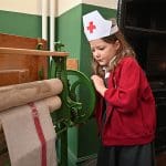 pupil dressed up in nurse hat while working an old fashioned clothing press