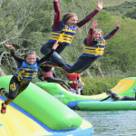 school group jumping of an inflatable object into the water on a lake