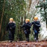 three school pupils running in a forest with hard hats and safety gear on
