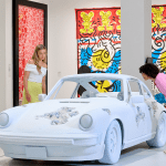 a white sculpture of a sports car in an exhibition room with students looking at it