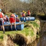 school trip group in harts had and life jackets by a river bank about to drop some man made rafts into the water