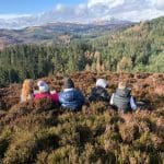 school trip group sitting on top of a hill outside surrounded with an amazing view of trees and distant slow lying mountain in Scotland