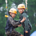 two primary school children on high ropes with hard hats and safety equipment on