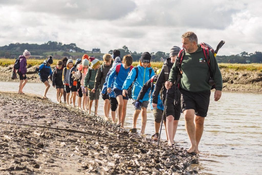 school pupils walking along a river with an environmentalist guide about river habitats