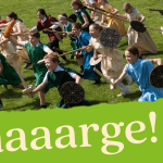 school children running in a field with Saxon dressing up clothes shields and wooden swords and spears
