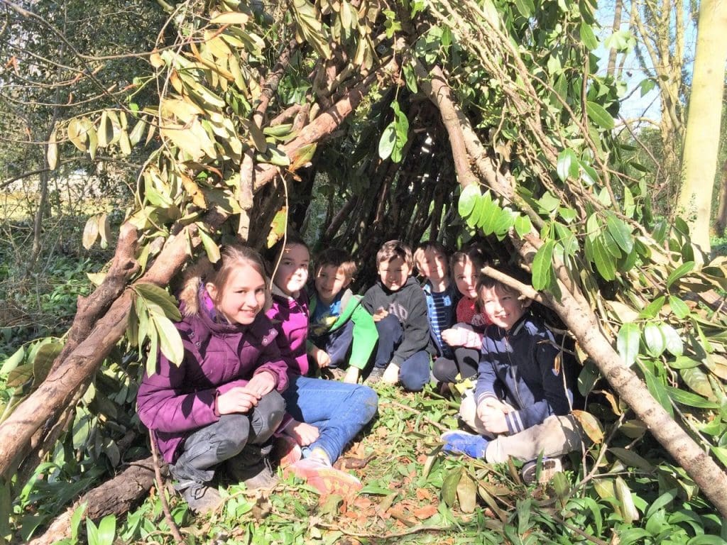 primary school students in forest made den of branches and leaves