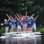 school group on a number of kayaks waving from a lake