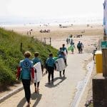 school pupils in wets suits walking down to the beach with surf boards