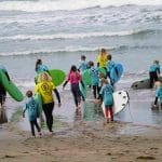school group at the beach carrying surf boards