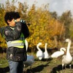 school pupil with binoculars looking at bird types in a river