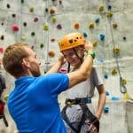school pupil with safety gear with hard hat ready to climb an outdoor climbing wall