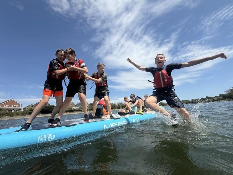 group of pupils jump off a giant paddle board into the water